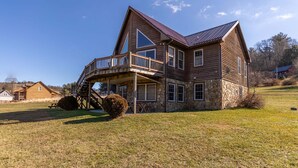 A large wooden house with a balcony, stone foundation, and a clear blue sky. - River House at Meadow Landing (Fleetwood)