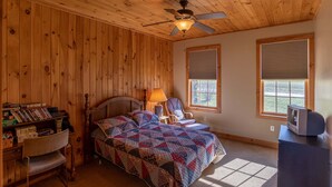 A wooden-paneled room with a bed, a desk, a chair, and a television. - River House at Meadow Landing (Fleetwood)