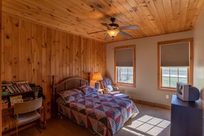 Ein Zimmer mit Holzwänden, einem Bett, einem Schreibtisch, einem Sessel und einem Fernseher.