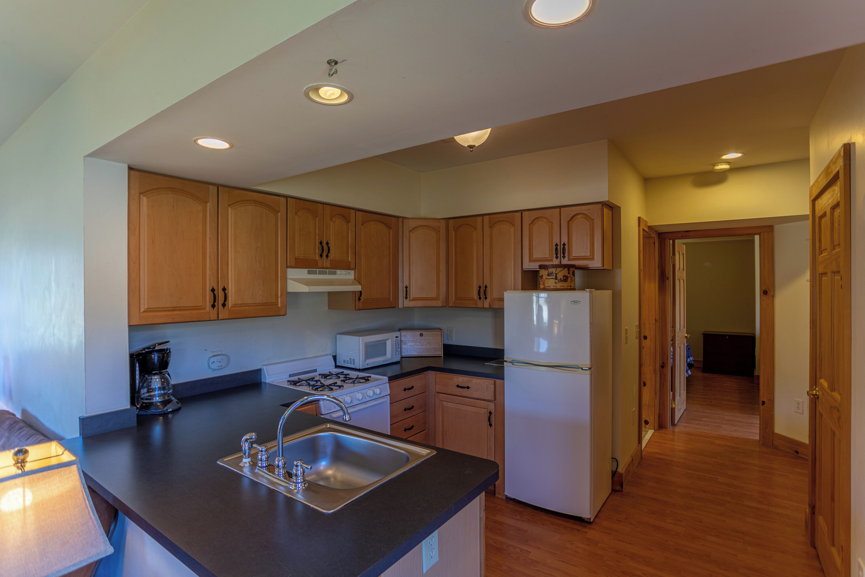 A kitchen with wooden cabinets, a sink, a stove, a microwave, and a refrigerator.