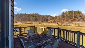 A wooden deck with a metal table and chairs, overlooking a grassy field and trees. - River House at Meadow Landing (Fleetwood)
