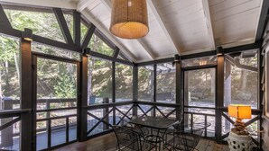 Un espacio de estar al aire libre cubierto con una mesa, sillas, ventanas amplias y una lámpara colgante.