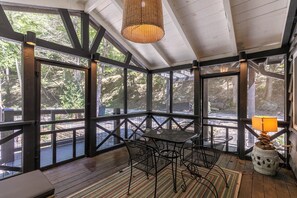 A covered outdoor seating area with a table and chairs, large windows, and a hanging light fixture. - Anglers Cottage (Blowing Rock)