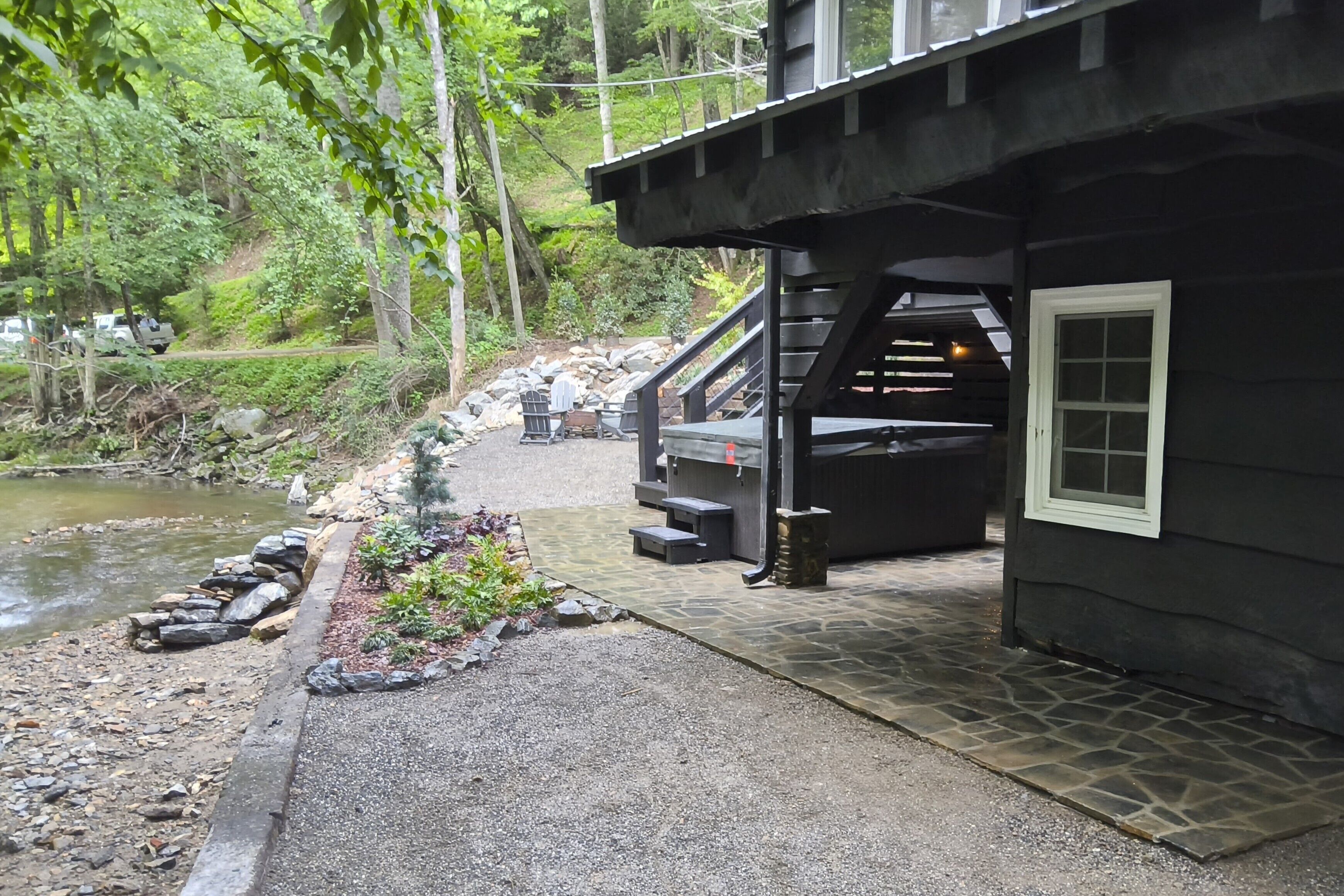 A cabin with a stone pathway leading to a dock over water, surrounded by greenery.