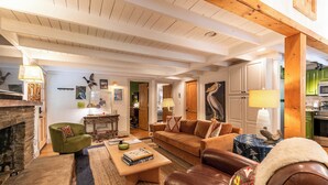 Una sala de estar acogedora con chimenea, un sillón verde, un sofá de cuero marrón y una mesa de centro con libros.