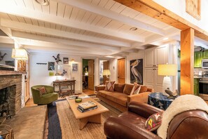 A cozy living room with a fireplace, a green armchair, a brown leather sofa, and a coffee table with books. - Anglers Cottage (Blowing Rock)