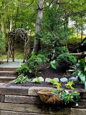 A garden with a wooden bench, a rustic arbor, and various plants. - Anglers Cottage (Blowing Rock)