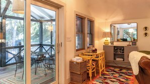Una habitación acogedora con una mesa de comedor, sillas, una cesta de mimbre, un sofá, un espejo y una ventana con persianas.