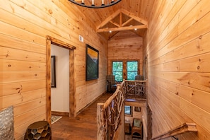 A wooden cabin interior with a staircase, a framed picture on the wall, and a window with a view of trees.
