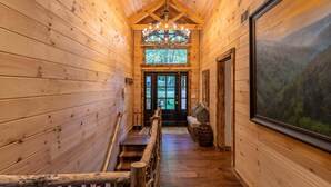 A wooden interior hallway with a chandelier, a bench, and a large framed picture on the wall. - Moosey Creek Lodge (Banner Elk)