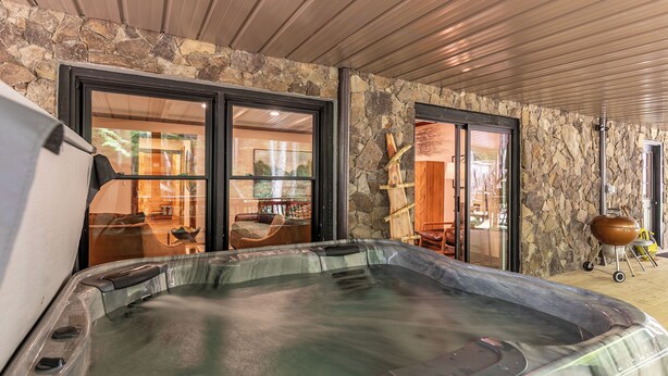 A hot tub in a stone-walled room with large sliding glass doors leading to a dining area. - Moosey Creek Lodge (Banner Elk)