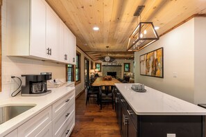 A modern kitchen with white cabinets, a wooden ceiling, a dining area with a large table, and a kitchen island.