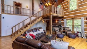 Ein geräumiger Wohnbereich mit einer Holztreppe, Ledersofas und einer hohen Decke mit freiliegenden Balken.