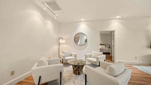 A modern living room with a round glass coffee table, white armchairs, a round mirror, and a visible door leading to another room. - Banner Elk Valley Overlook (Banner Elk)