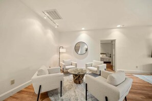 A modern living room with a round glass coffee table, white armchairs, a round mirror, and a visible door leading to another room. - Banner Elk Valley Overlook (Banner Elk)