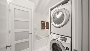 A laundry room with stacked washers and dryers, a white door, and a small window. - Banner Elk Valley Overlook (Banner Elk)