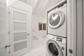 A laundry room with stacked washers and dryers, a white door, and a small window. - Banner Elk Valley Overlook (Banner Elk)