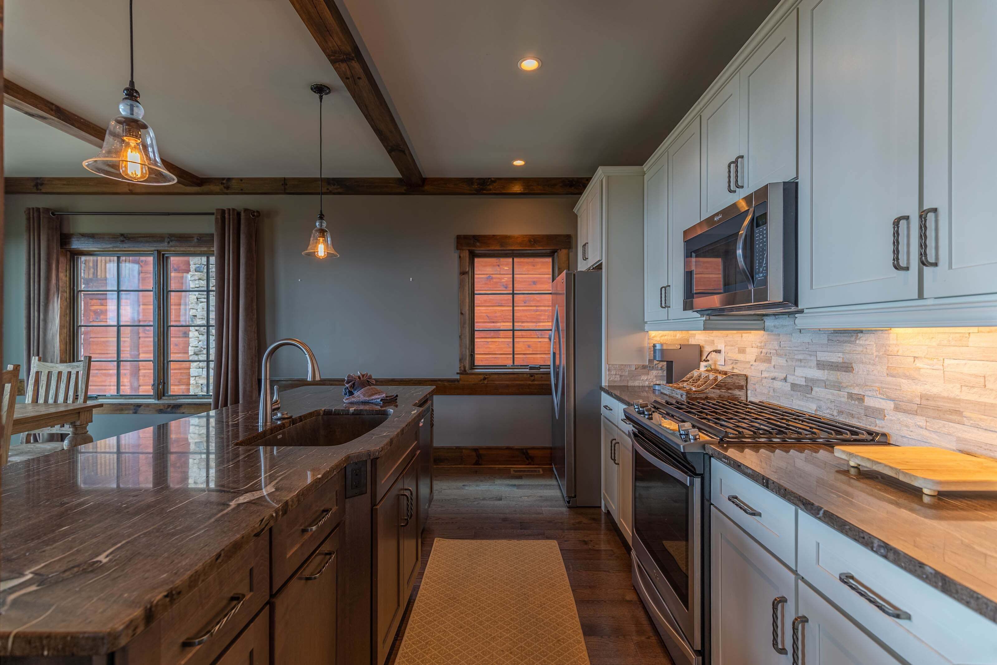 A kitchen with a large island, stainless steel appliances, and a stone backsplash.