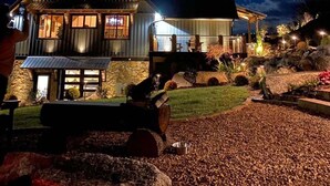 Una casa de dos pisos con fachada de piedra, una terraza de madera y un patio delantero bien iluminado.