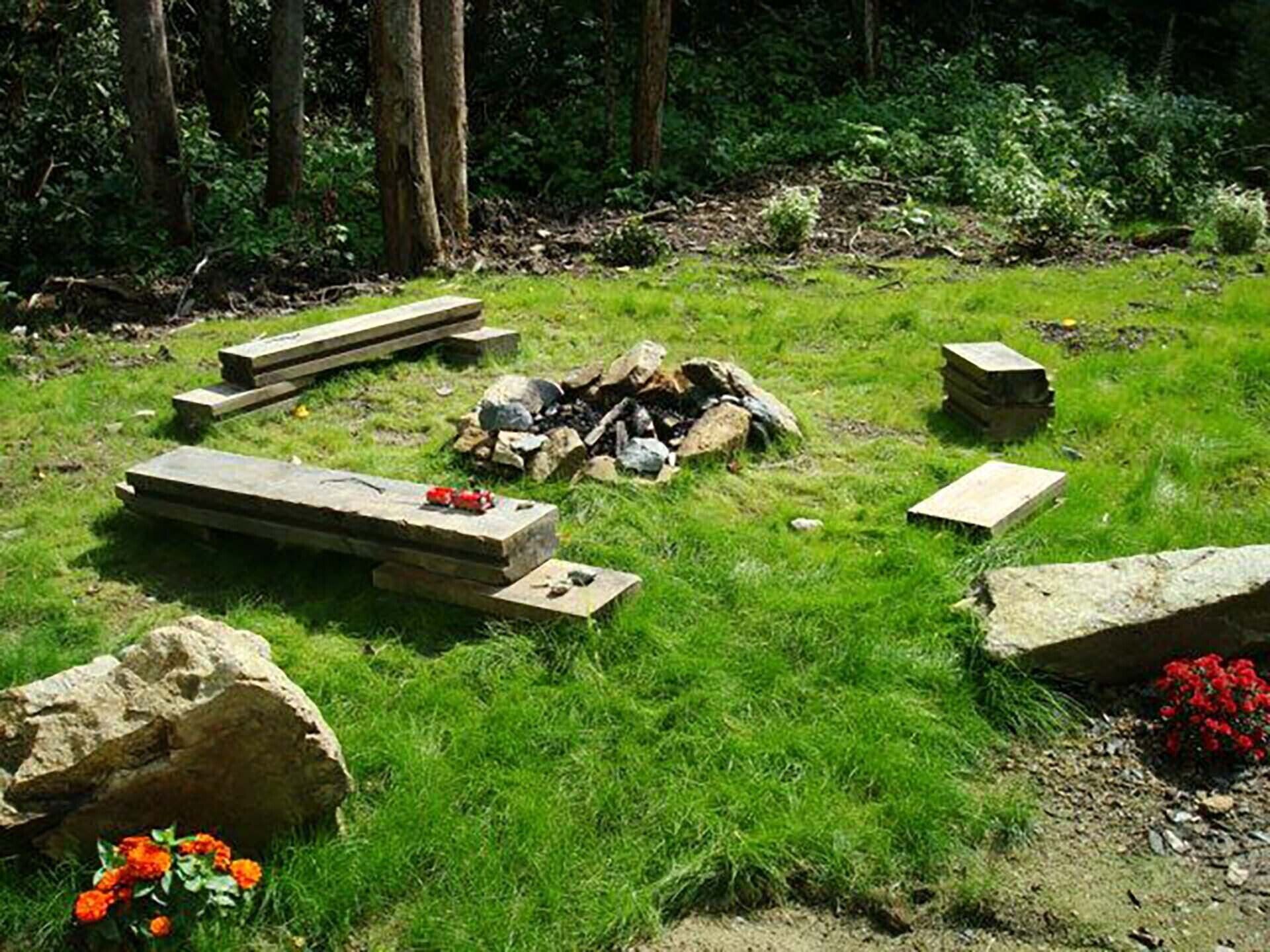 En kirkegård med stenbænke og gravsten, omgivet af græs og træer.