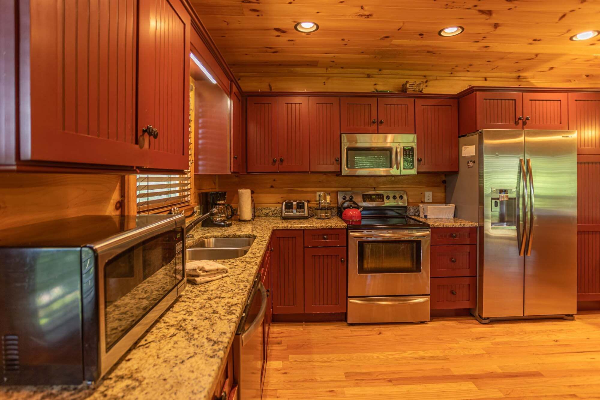 Una cocina con armarios de madera, electrodomésticos de acero inoxidable, encimeras de granito y suelo de madera.