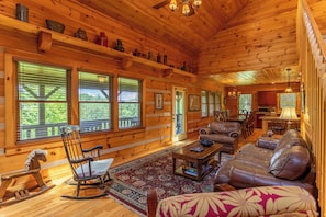 Interior de cabana de tronco com sala de jantar, sala de estar com mobiliário de couro e cozinha.