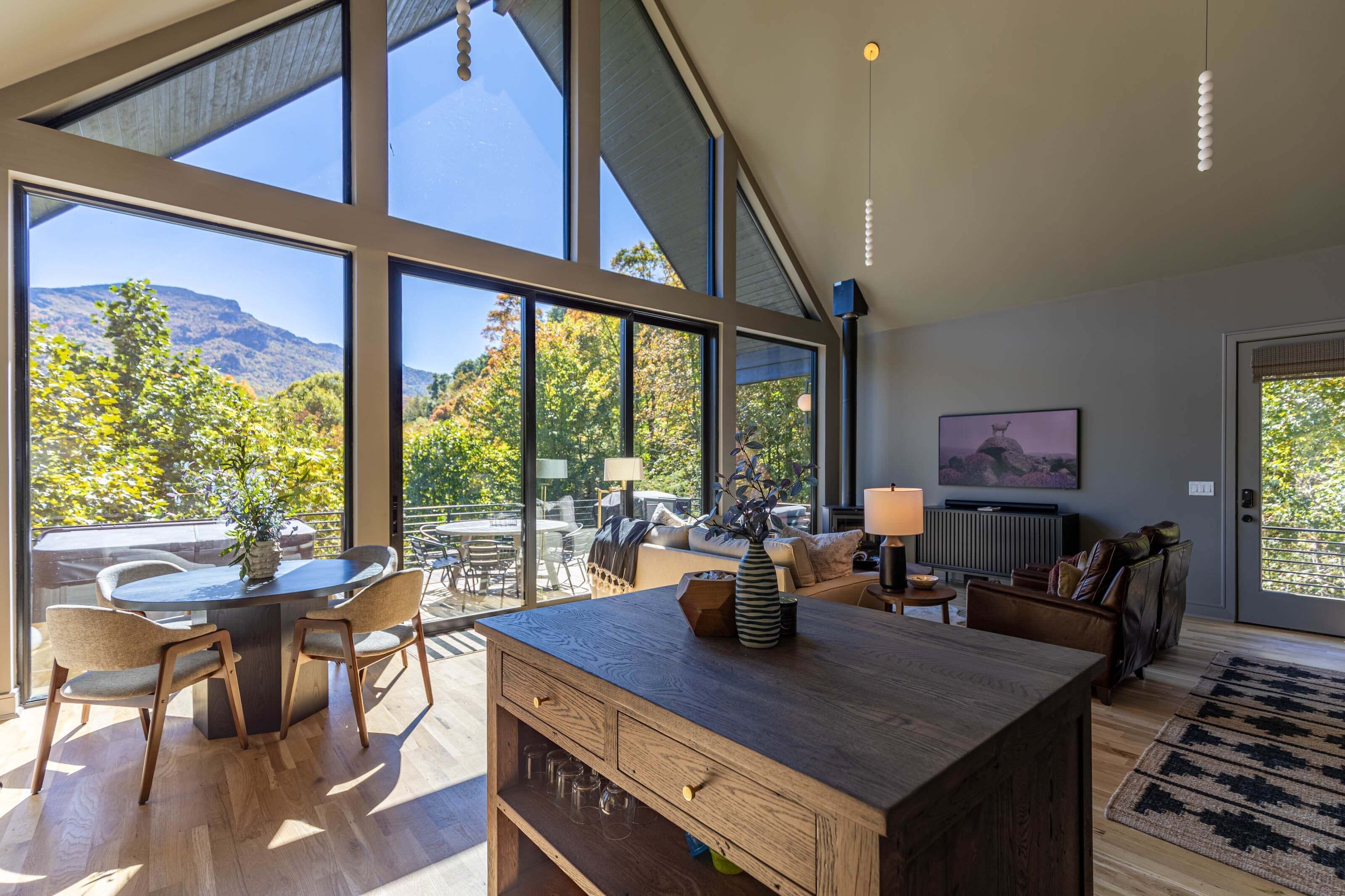 A spacious room with large windows, a wooden dining table, and a cozy seating area.