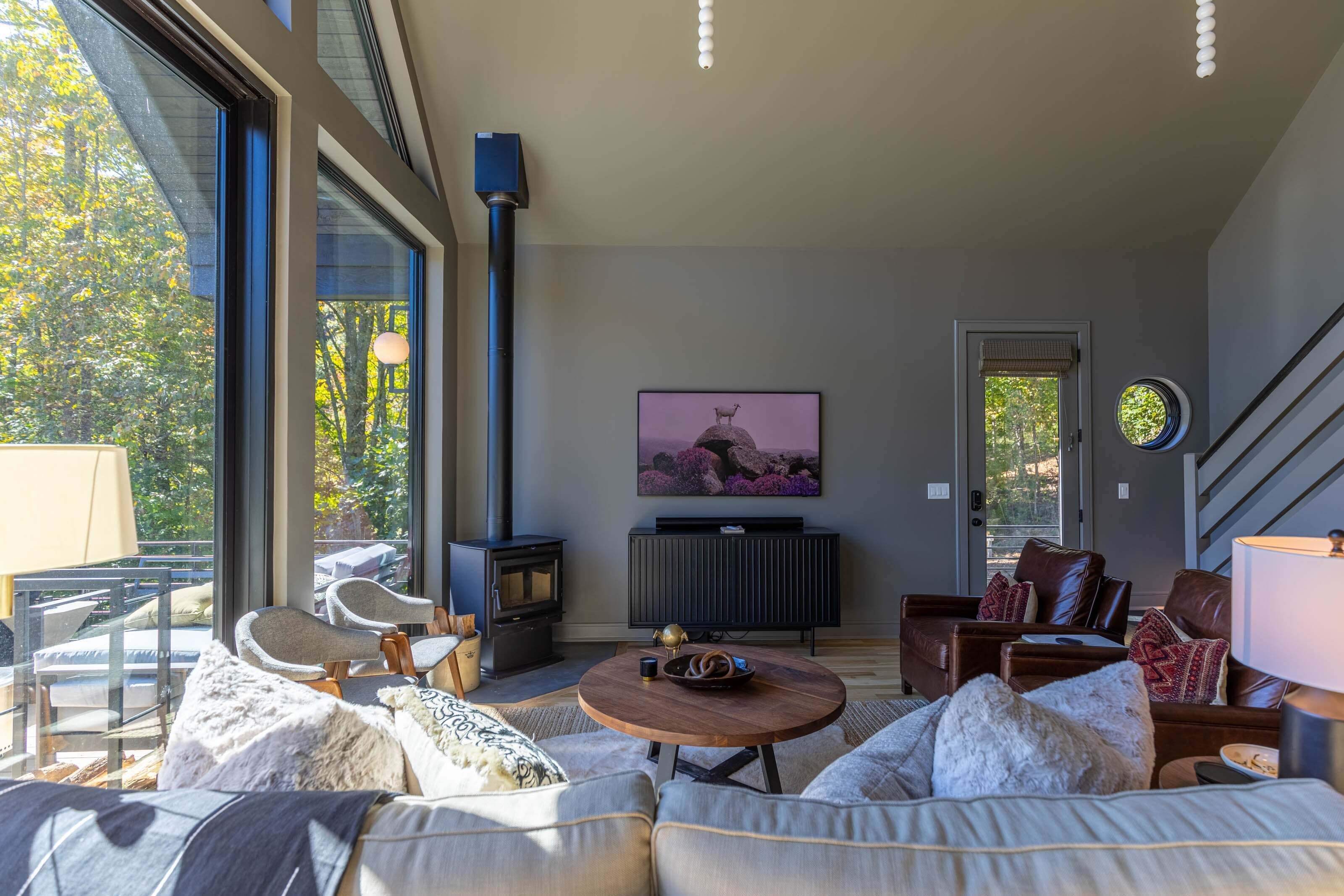 A modern living room with a fireplace, comfortable seating, and a large window offering a view of trees.