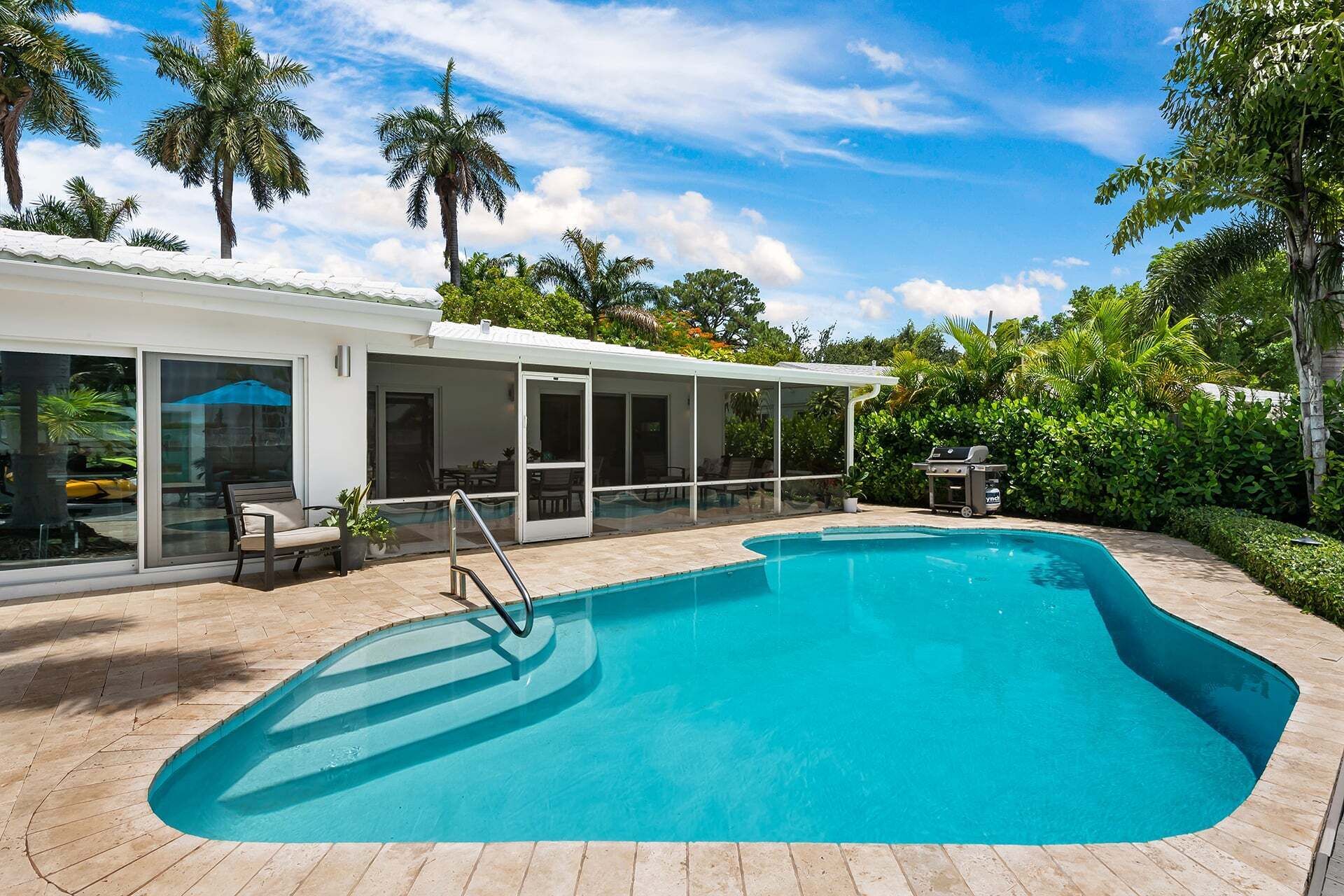 Ein Pool mit überdachter Terrasse, umgeben von Palmen und viel Grün.