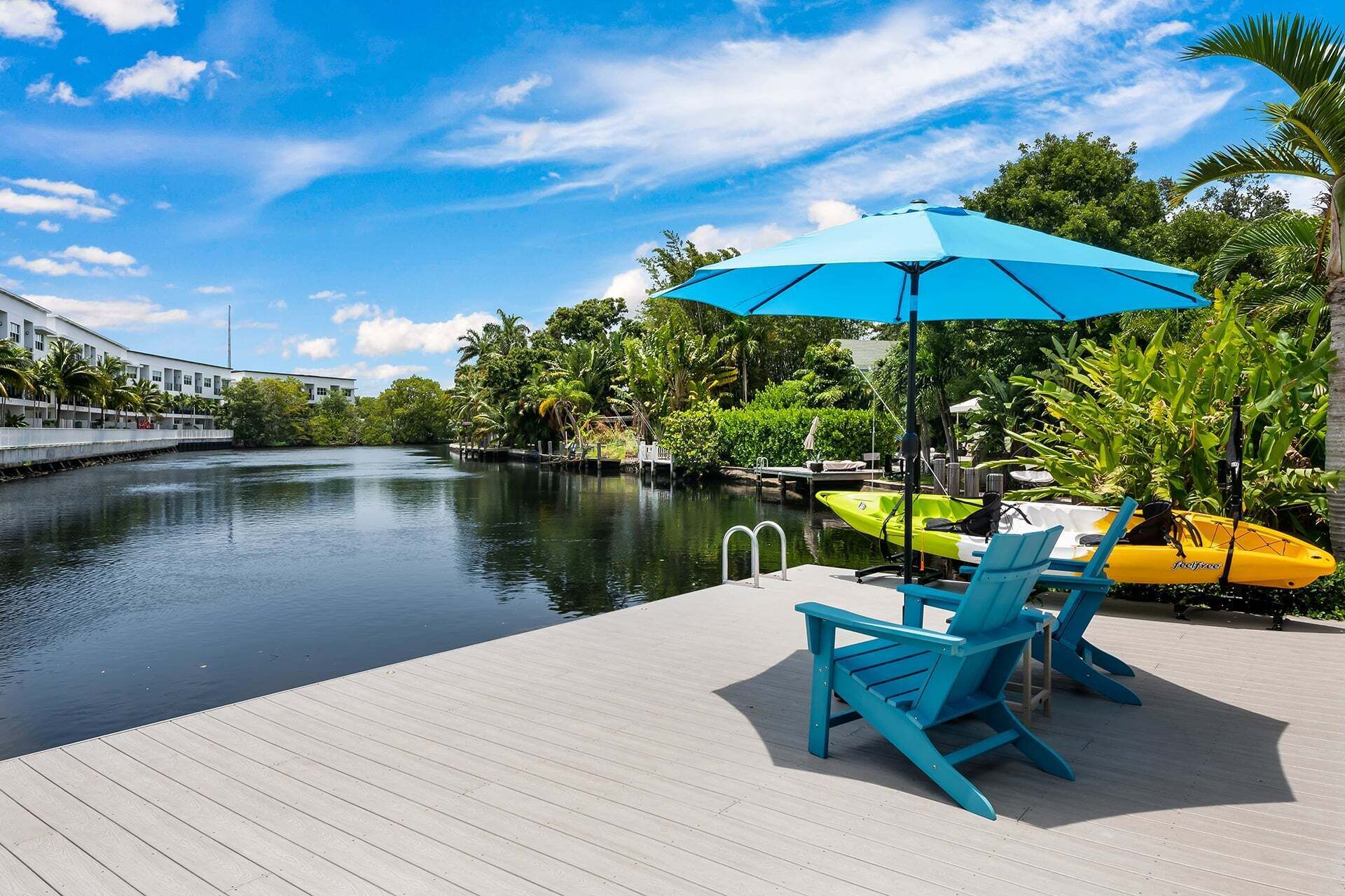 A wooden dock with chairs and a blue umbrella, a calm river, and lush greenery.