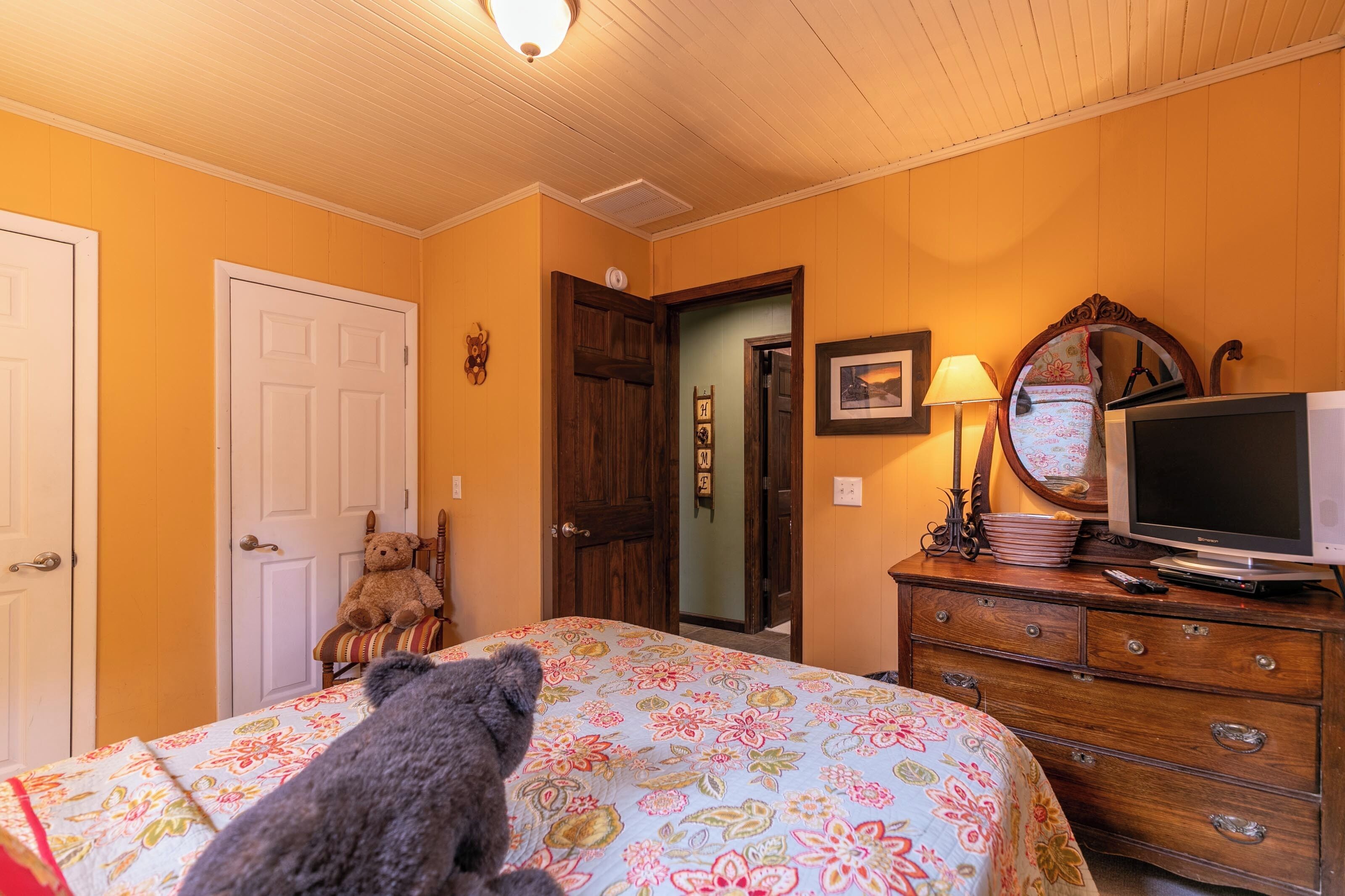 A bedroom with a bed, dresser, television, and teddy bears.