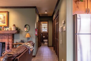 Un couloir étroit avec une cheminée, un canapé, un réfrigérateur et une porte donnant sur une salle de bain.