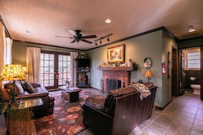 A living room with a fireplace, a ceiling fan, and a television.