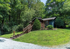 A cabin with a wooden staircase leading to a deck, surrounded by lush greenery.