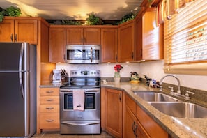 A kitchen with wooden cabinets, stainless steel appliances, a granite countertop, and a window with blinds.