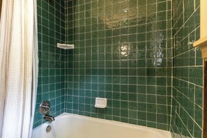 Une salle de bain avec des carreaux verts, une baignoire blanche et un rideau de douche.