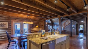 A log cabin interior with a kitchen, dining area, and a staircase leading to another level. - Highland Mist (Banner Elk)