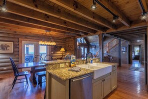 A log cabin interior with a kitchen, dining area, and a staircase leading to another level. - Highland Mist (Banner Elk)
