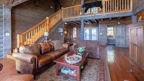 A log cabin interior with a wooden staircase, leather furniture, and a black bear on the upper level. - Highland Mist (Banner Elk)