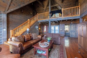 A log cabin interior with a wooden staircase, leather furniture, and a black bear on the upper level. - Highland Mist (Banner Elk)