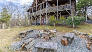 A rustic cabin with a stone fireplace, wooden deck, and a stone pathway leading to the entrance. - Highland Mist (Banner Elk)