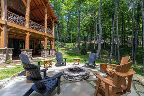 An outdoor patio with Adirondack chairs, a stone fire pit, and a wooden deck overlooking a forested area. - Bear Creek Cabin at Eagles Nest (Banner Elk)