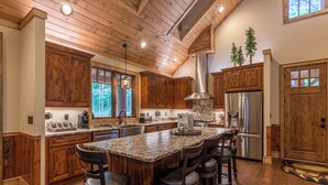 A spacious kitchen with wooden cabinets, a large island with bar stools, stainless steel appliances, and a vaulted ceiling. - Bear Creek Cabin at Eagles Nest (Banner Elk)