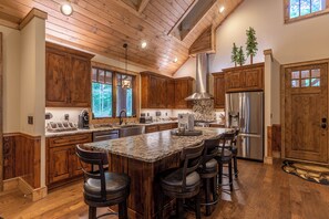 A spacious kitchen with wooden cabinets, a large island with bar stools, stainless steel appliances, and a vaulted ceiling. - Bear Creek Cabin at Eagles Nest (Banner Elk)