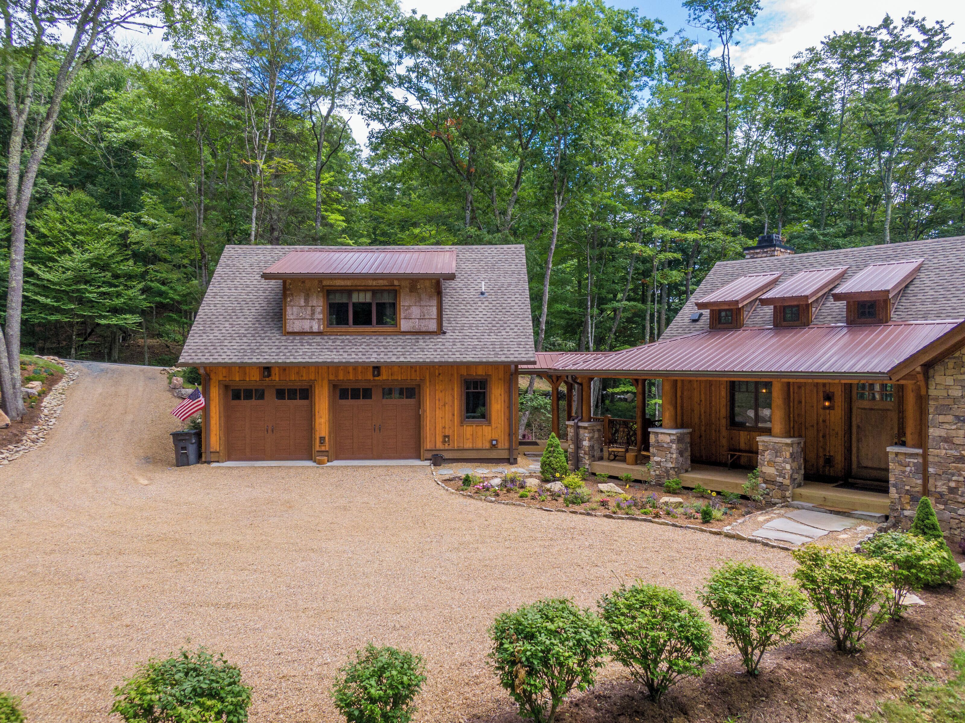 A two-story log cabin with a gravel driveway and a stone patio.