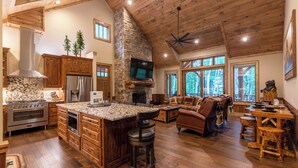 A spacious kitchen with a large island, wooden cabinets, and a stone fireplace. - Bear Creek Cabin at Eagles Nest (Banner Elk)