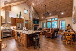 A spacious kitchen with a large island, wooden cabinets, and a stone fireplace. - Bear Creek Cabin at Eagles Nest (Banner Elk)