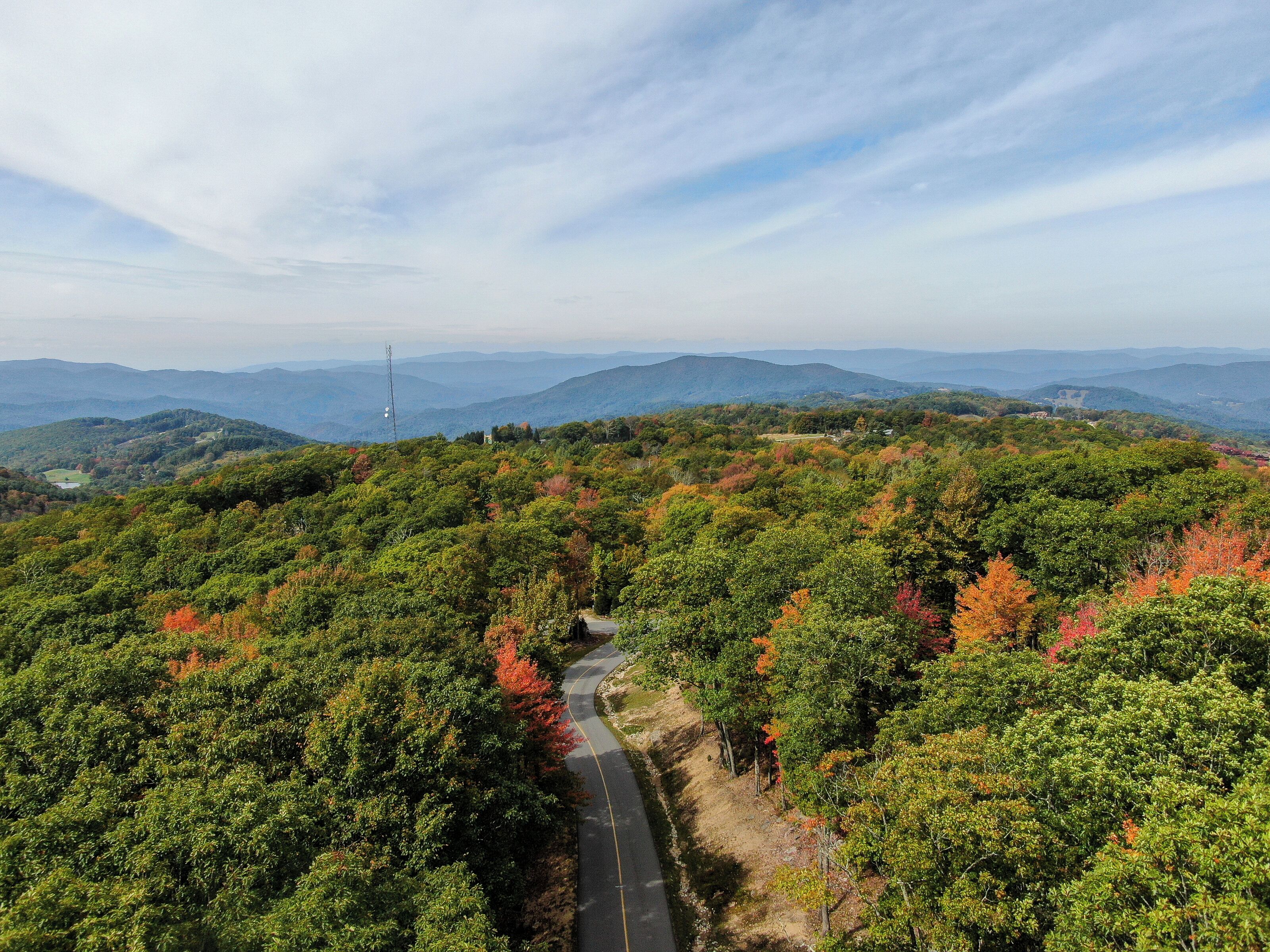 A winding road through a forested mountain area with distant mountain ranges.