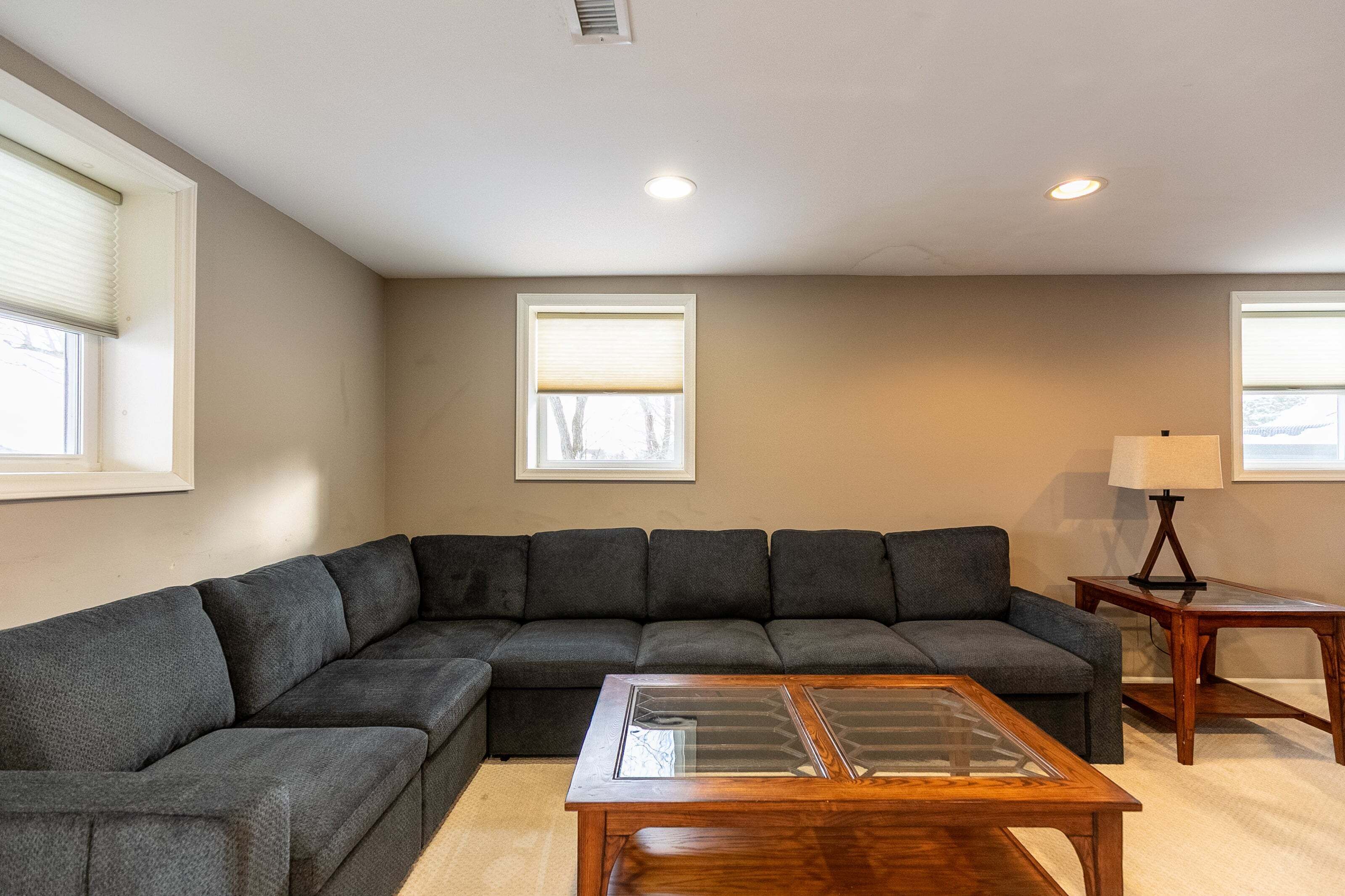 A living room with a sectional sofa, a glass-top coffee table, and a lamp on a side table.
