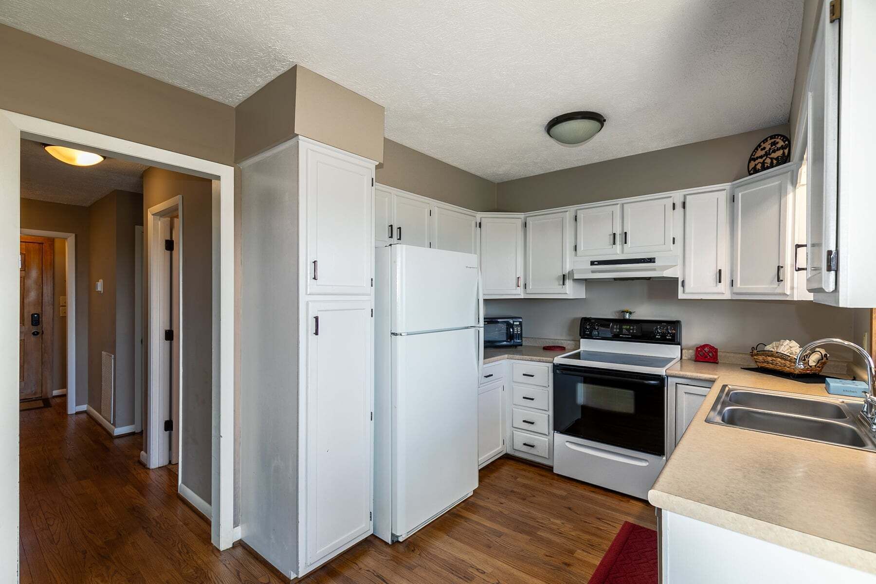 A compact kitchen with white cabinets, a refrigerator, a microwave, an oven, and a sink.